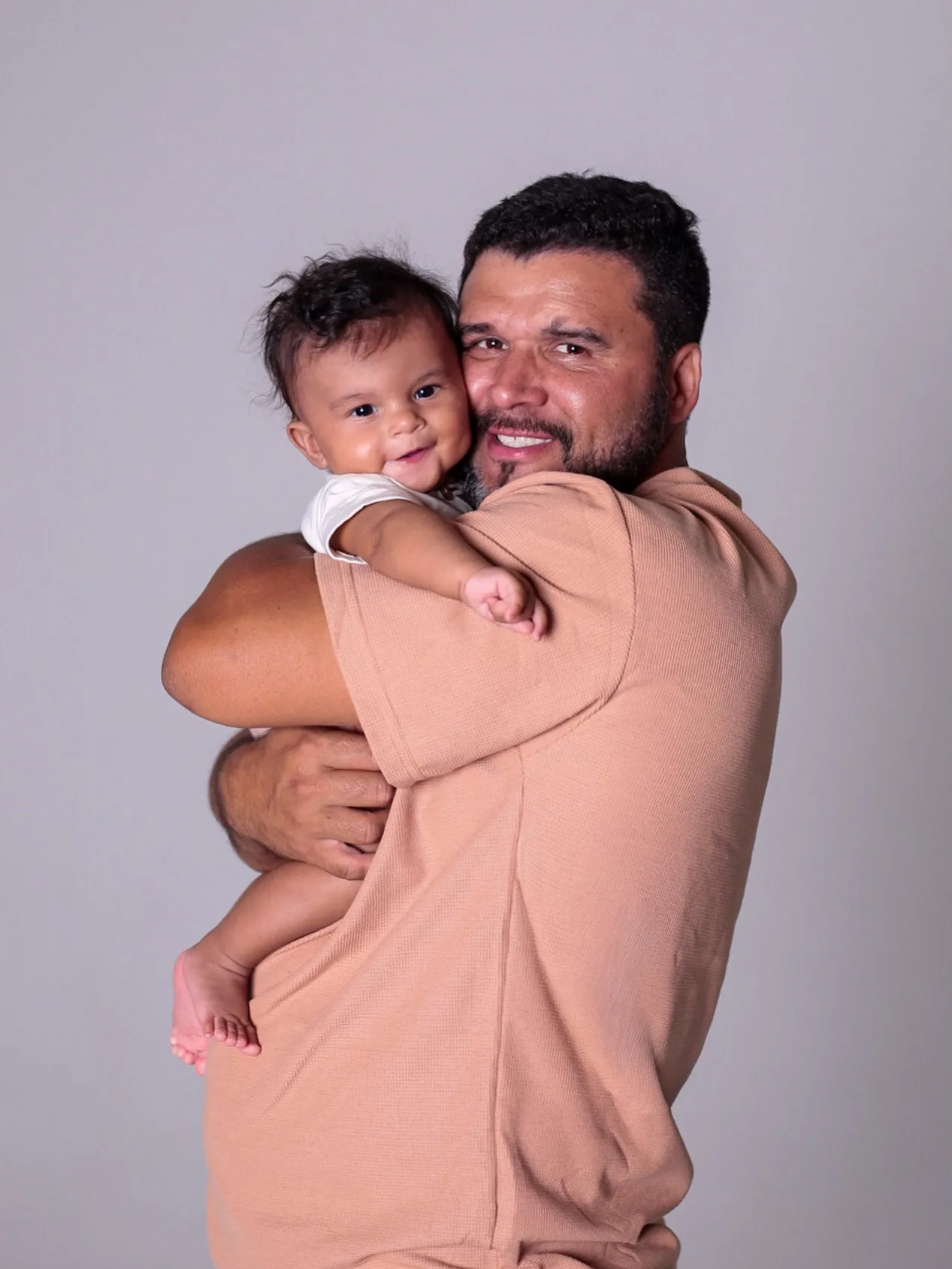 Pai abraça o bebê junto ao rosto.