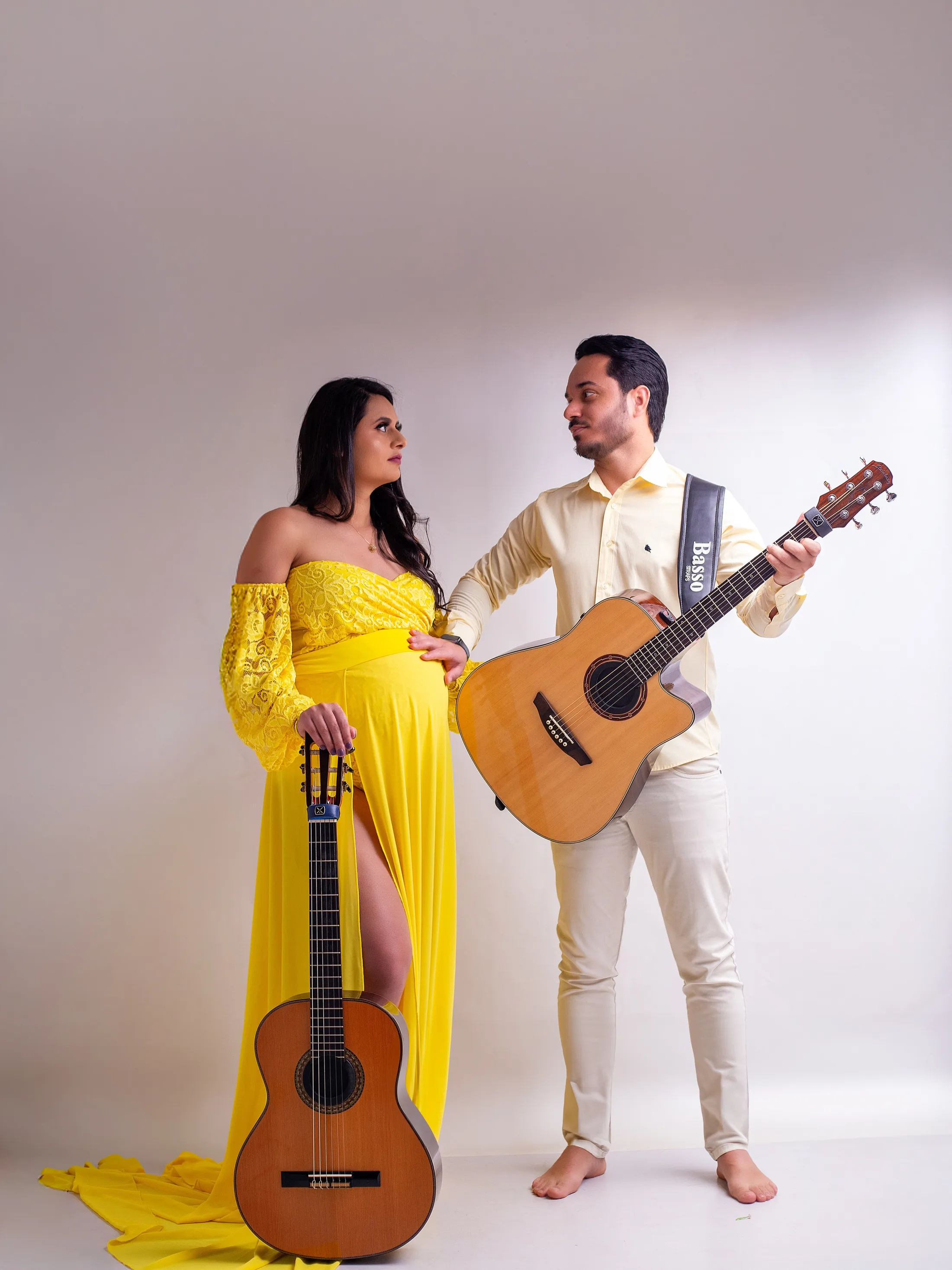 Gestante de vestido amarelo e homem com violão, em fundo cinza-claro.