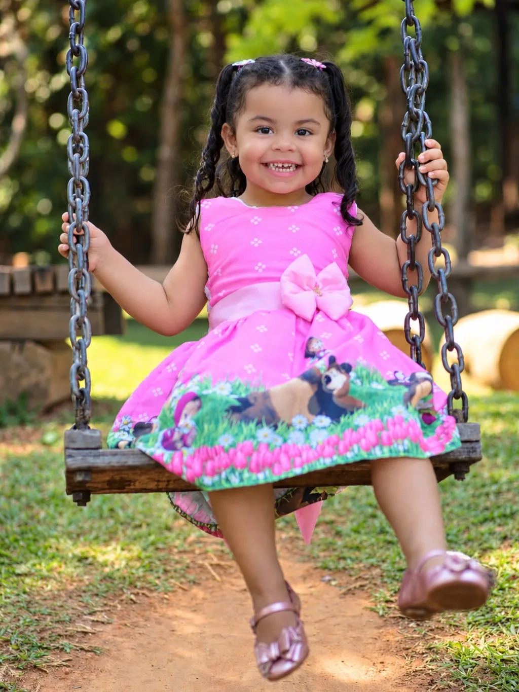 Menina de vestido rosa sorri sentada em um balanço.