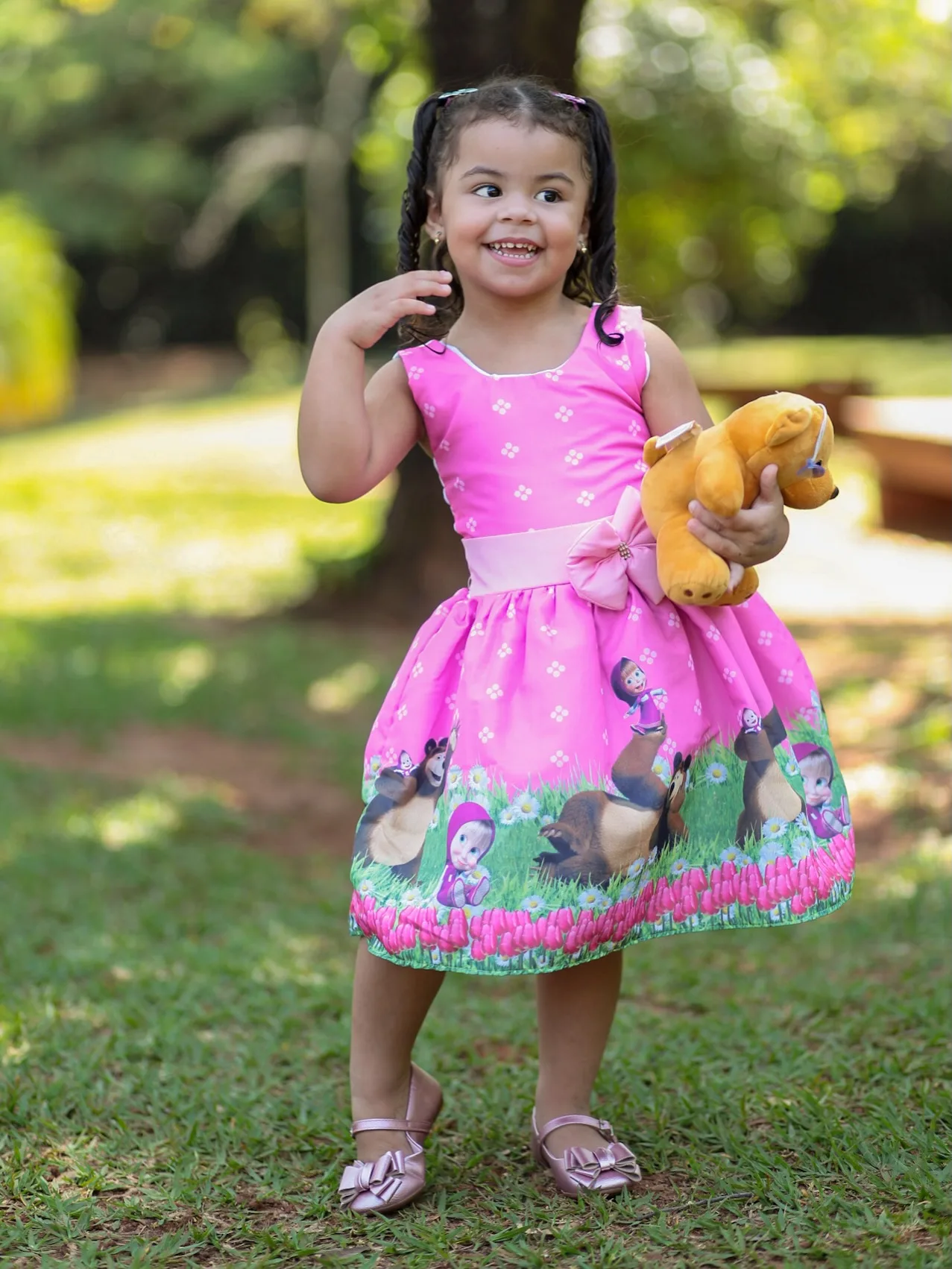Menina de vestido rosa segura um ursinho em um jardim.