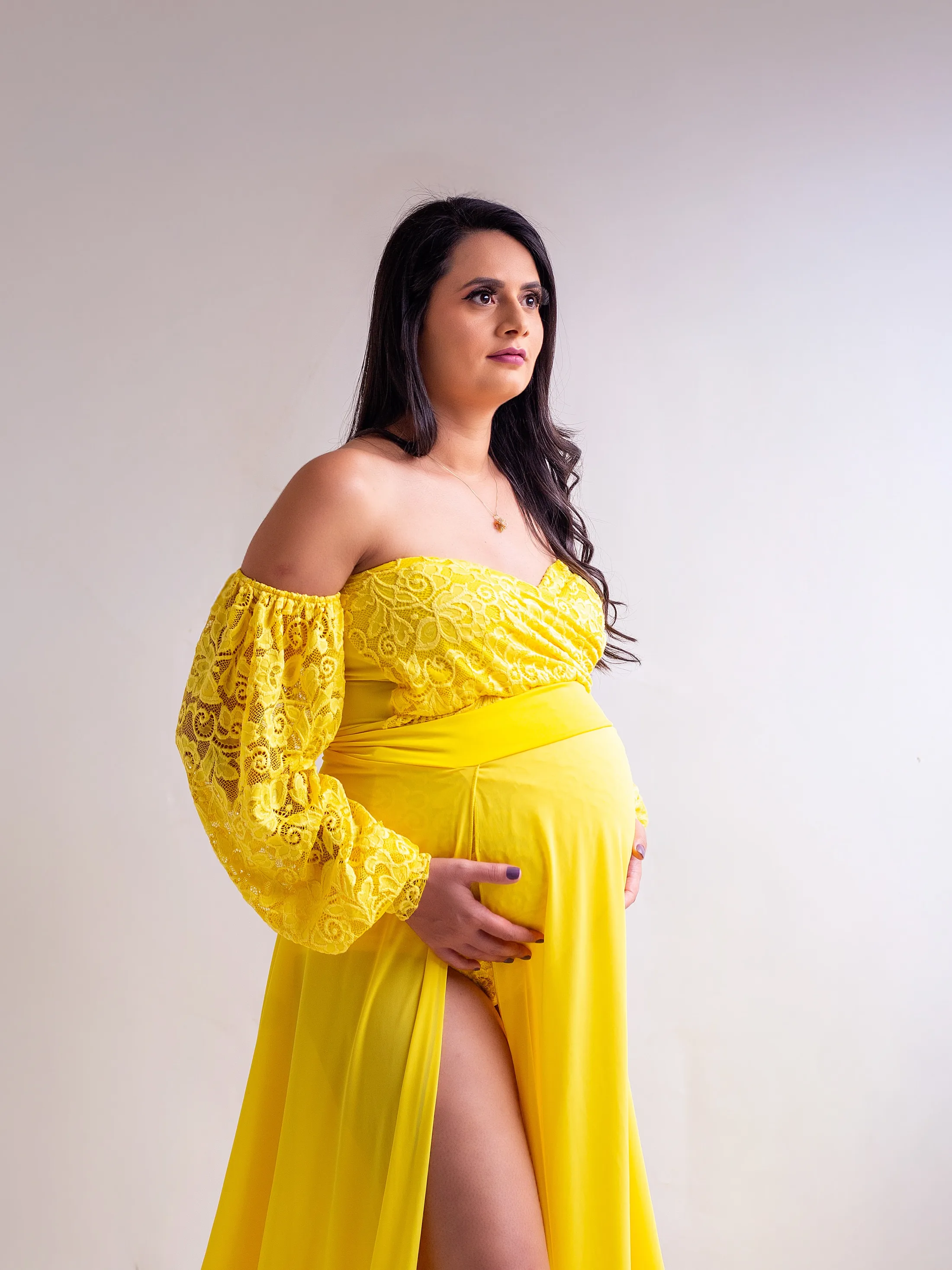 Gestante de vestido amarelo com renda nos braços, em retrato de meio corpo.