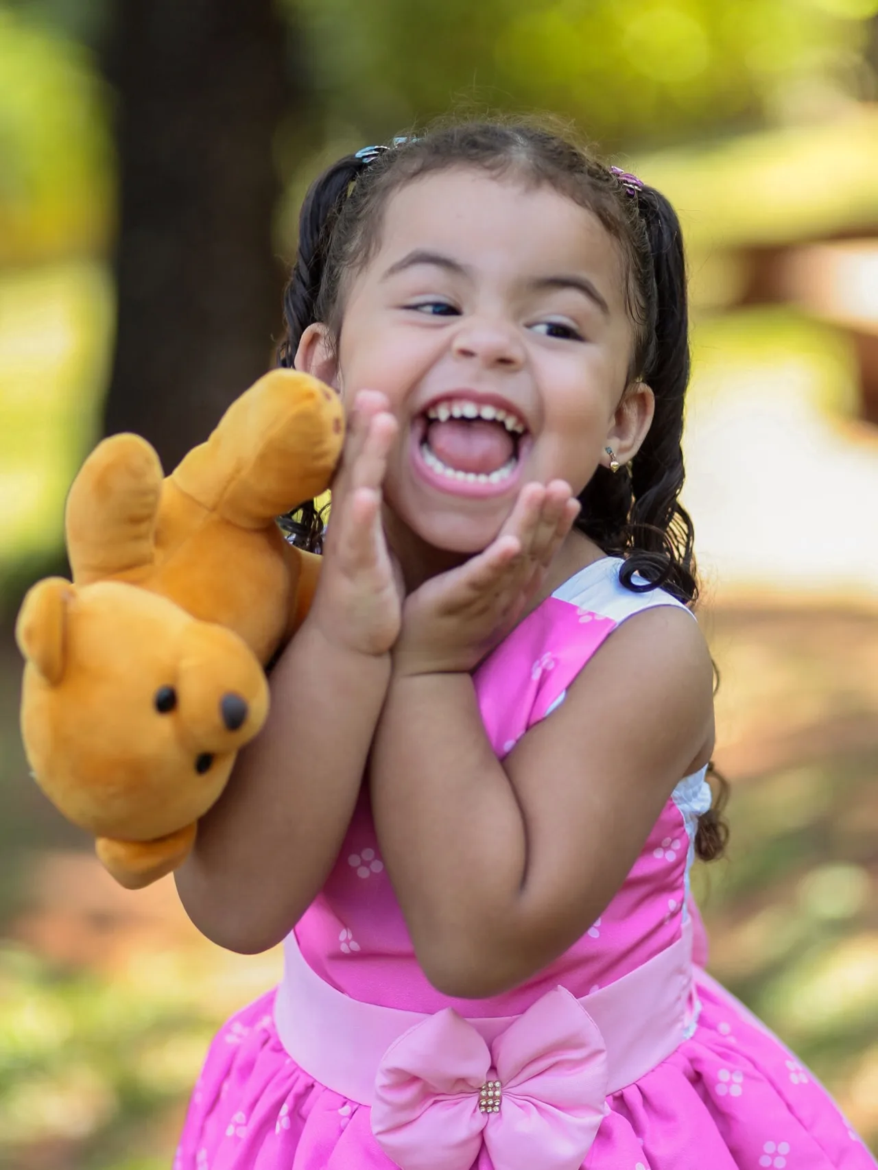 Menina ri com um ursinho junto ao rosto.