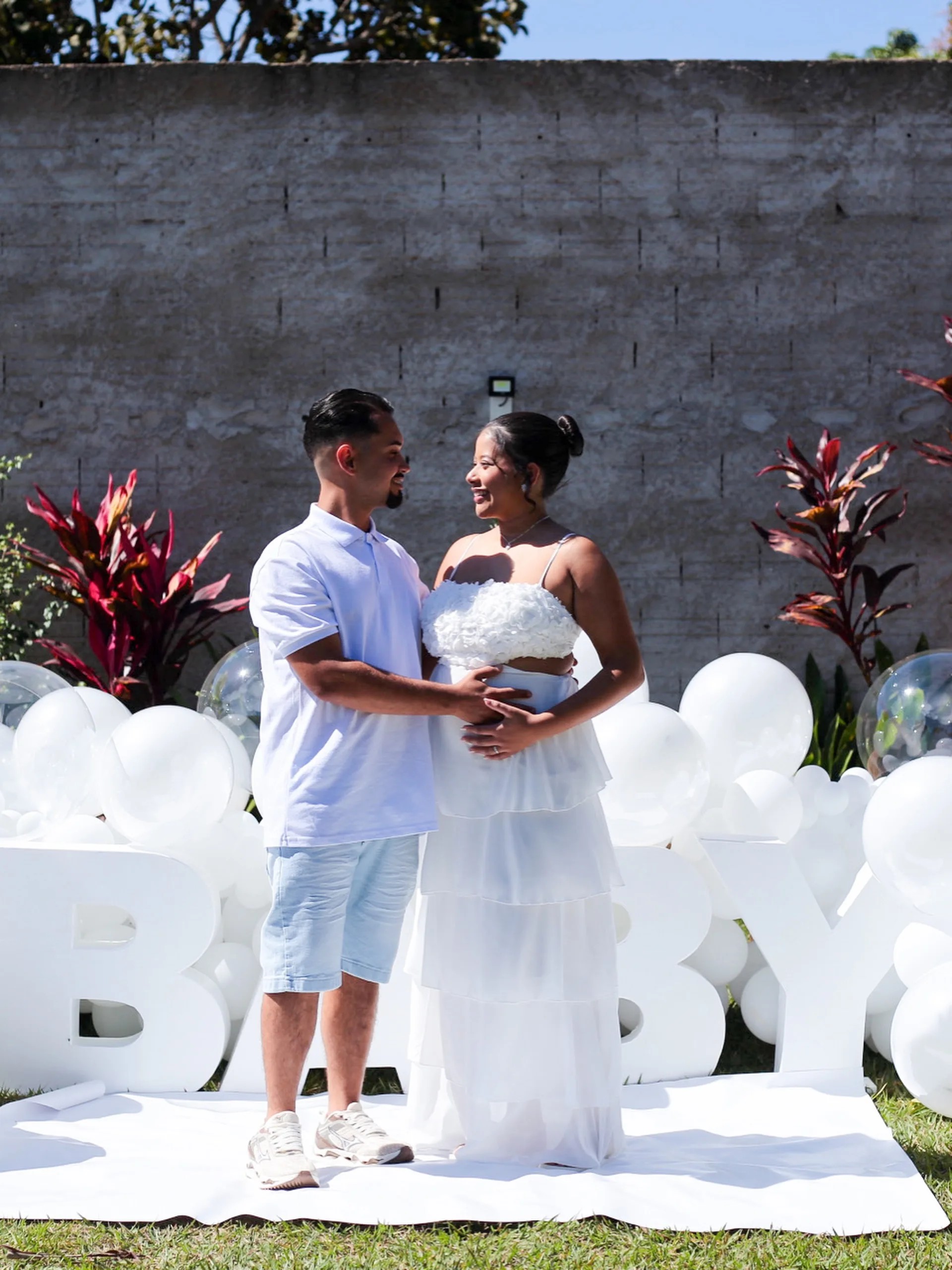 Casal de branco diante de letras e balões brancos que formam a palavra BABY.
