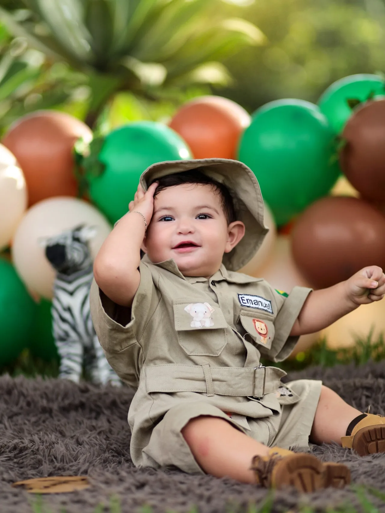 Menino de chapéu e roupa de safári leva a mão à cabeça, entre balões.