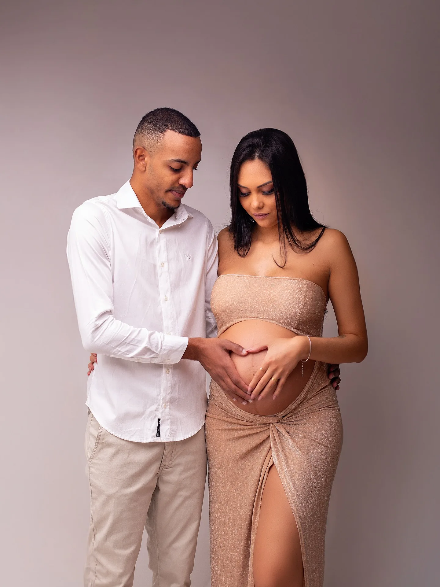 Casal com as mãos sobre a barriga da gestante, em fundo cinza.