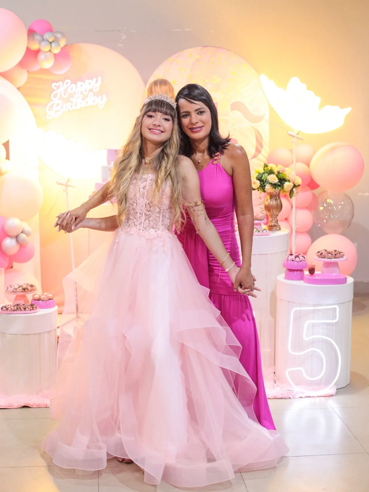 Debutante de vestido rosa armado ao lado de uma mulher de vestido pink.