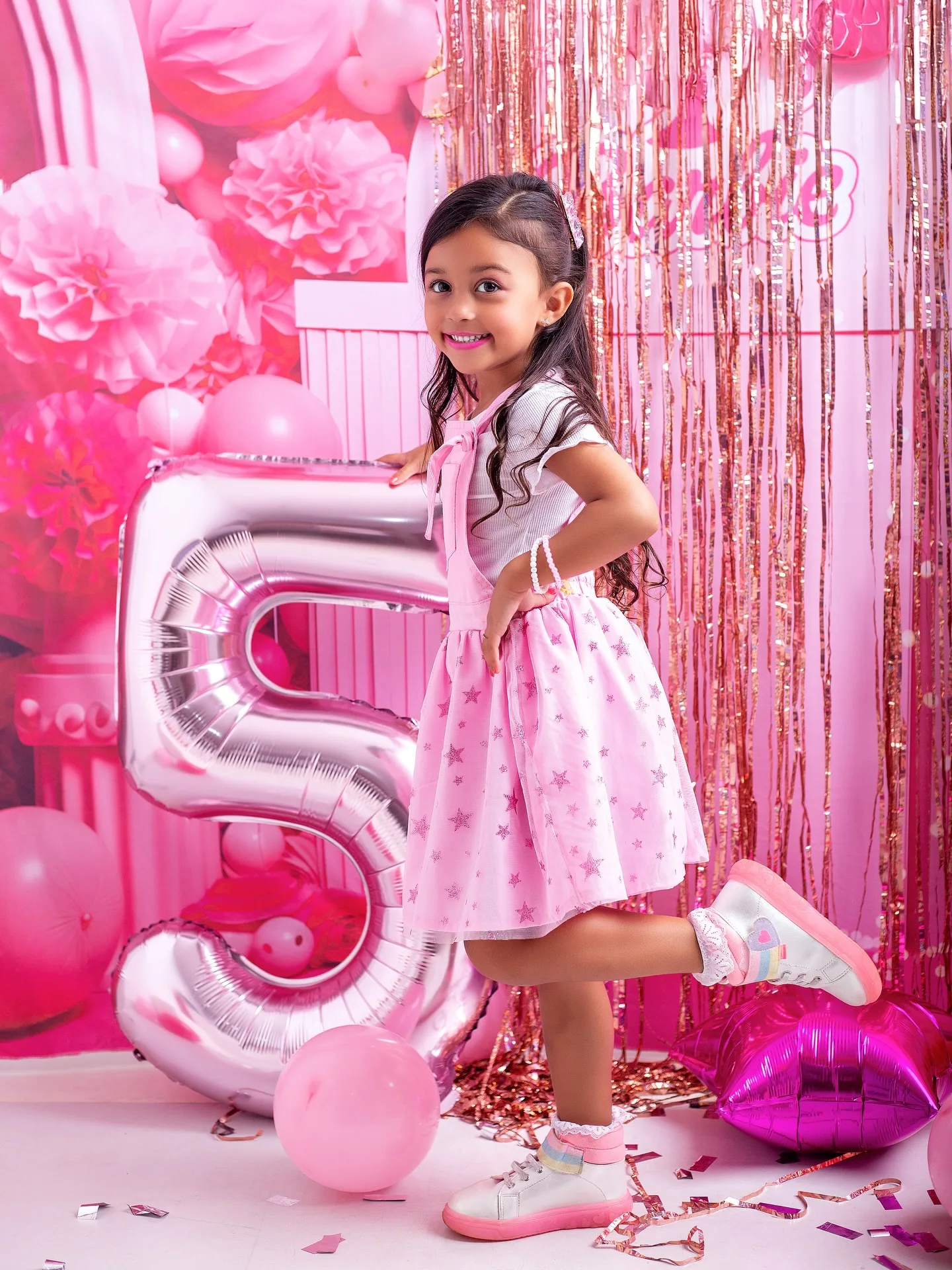 Menina com a mão na cintura ao lado de um balão prateado de número 5.
