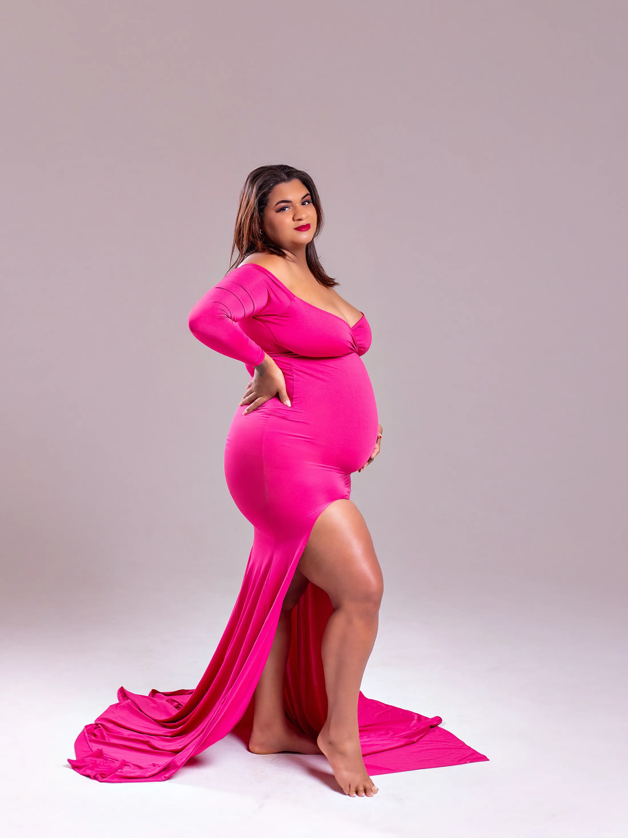 Gestante de vestido pink com cauda, de perfil, com a mão na barriga.