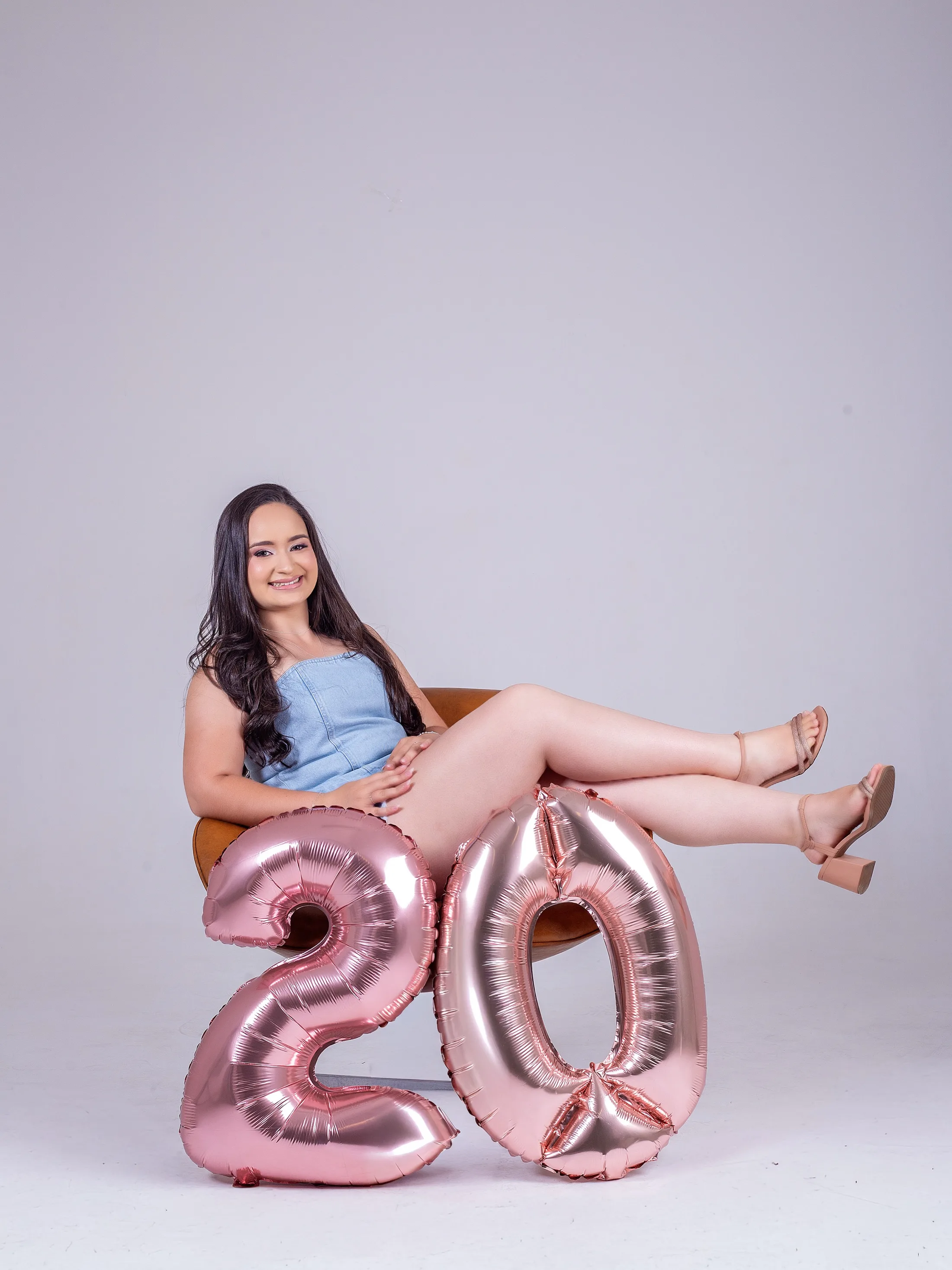 Jovem sentada em uma poltrona com balões de número 20 à frente.