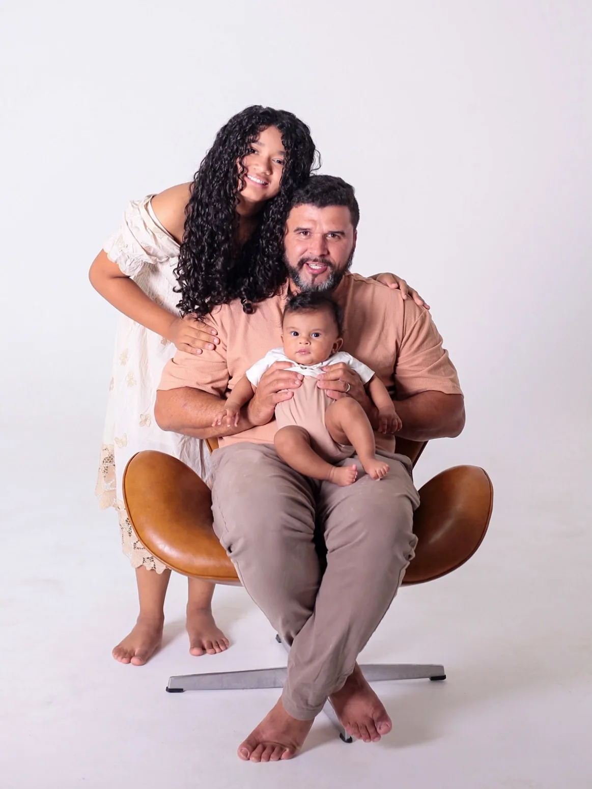 Pai sentado com o bebê no colo e a filha atrás, abraçando-o.