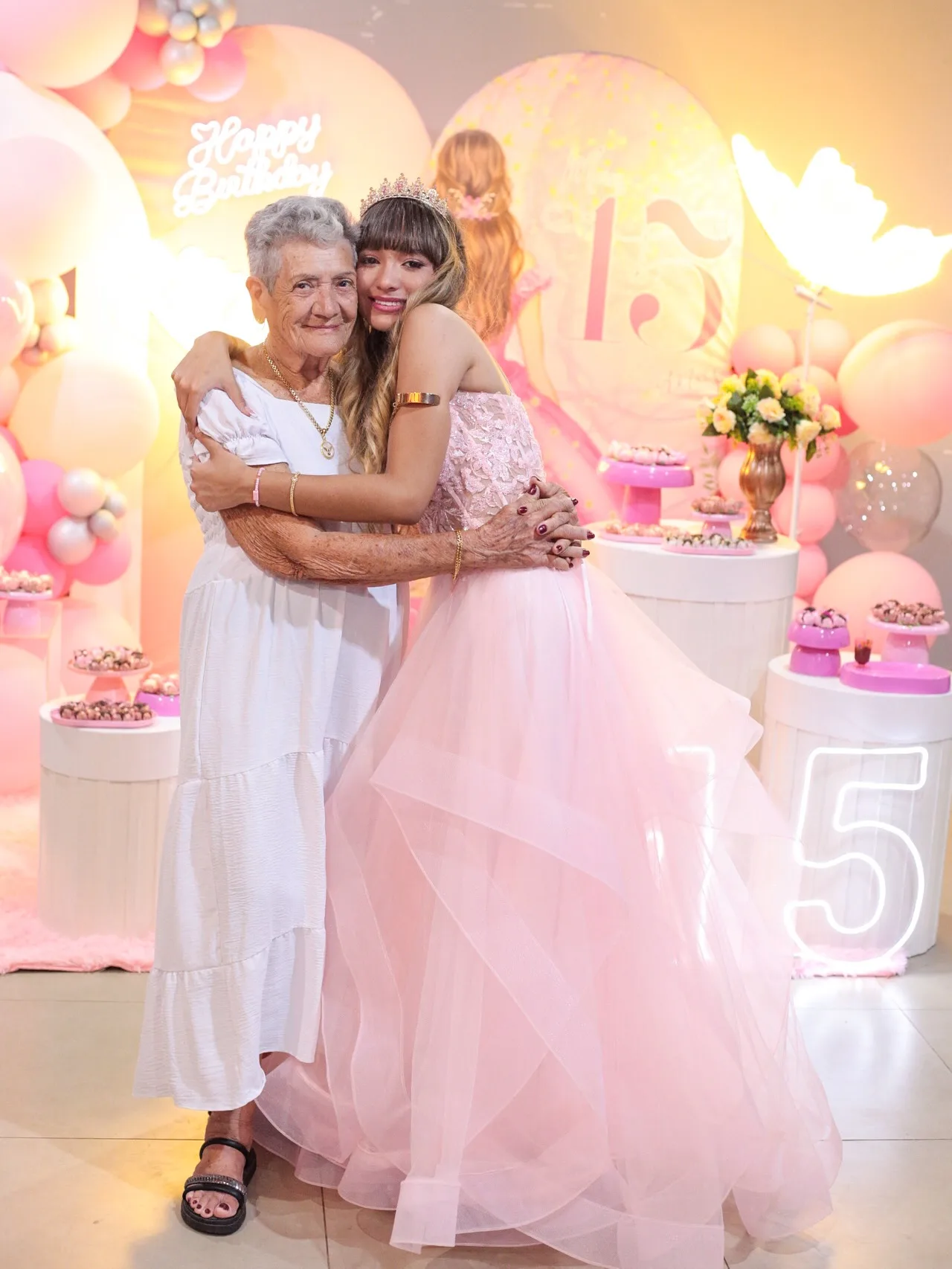 Debutante abraça uma senhora de vestido branco na festa de 15 anos.