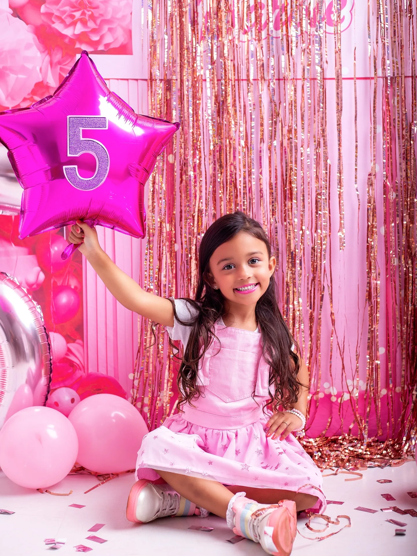 Menina segura um balão rosa em forma de estrela com o número 5.