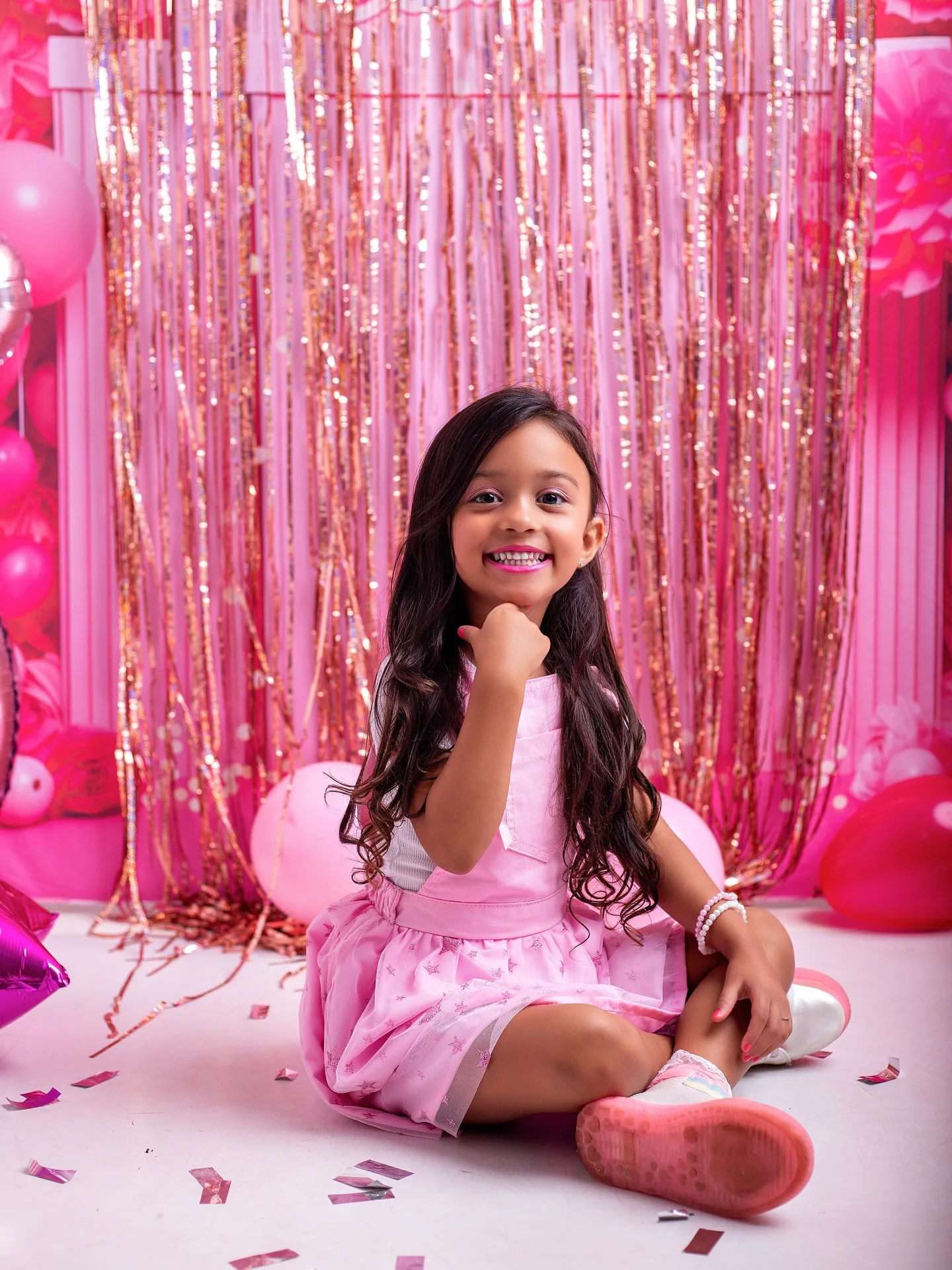 Menina sentada no chão com a mão no queixo, em cenário rosa.