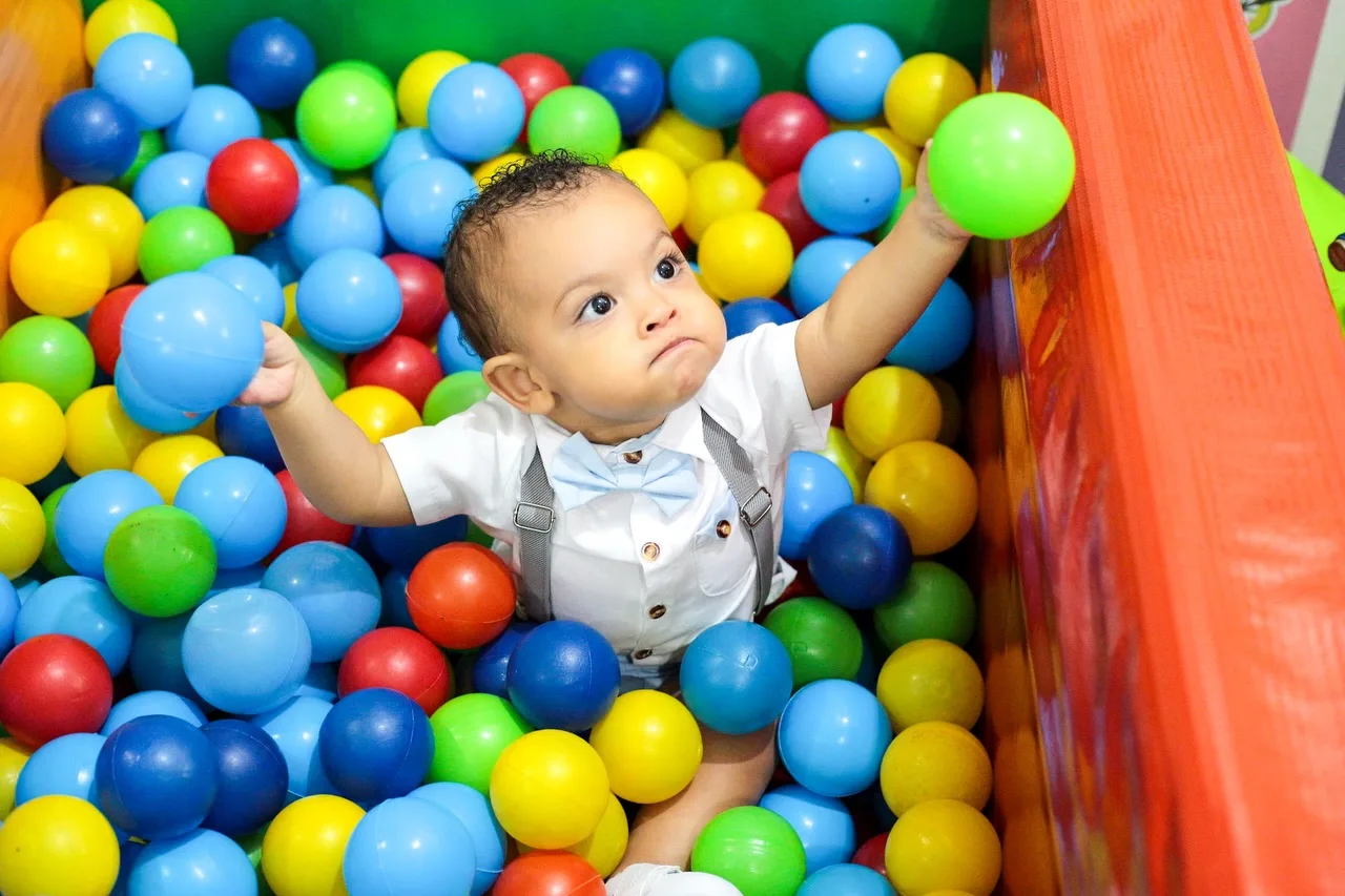 Menino aniversariante estende a mão para pegar uma bolinha na piscina de bolinhas.
