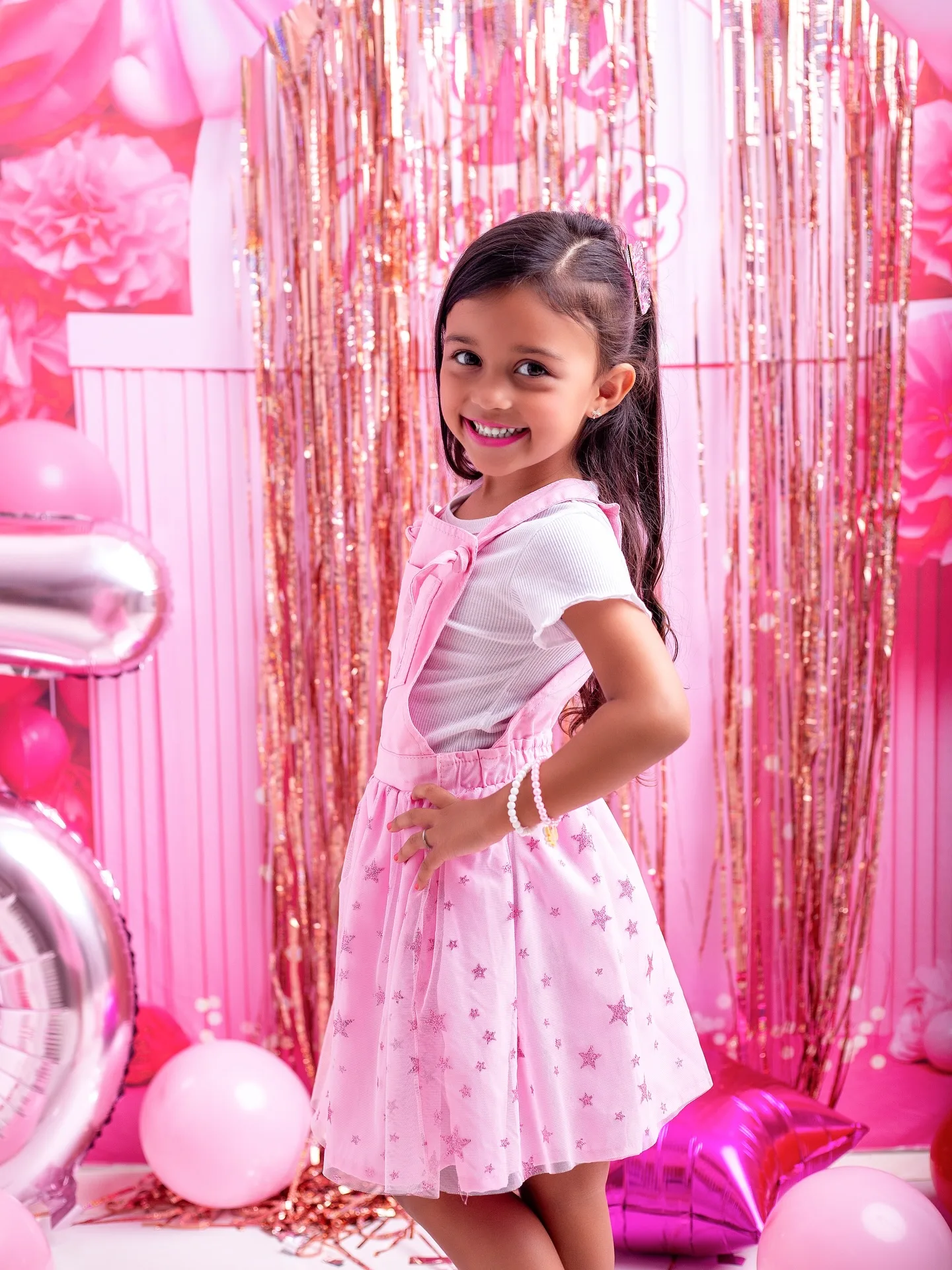Menina de vestido rosa posa de lado, com a mão na cintura.