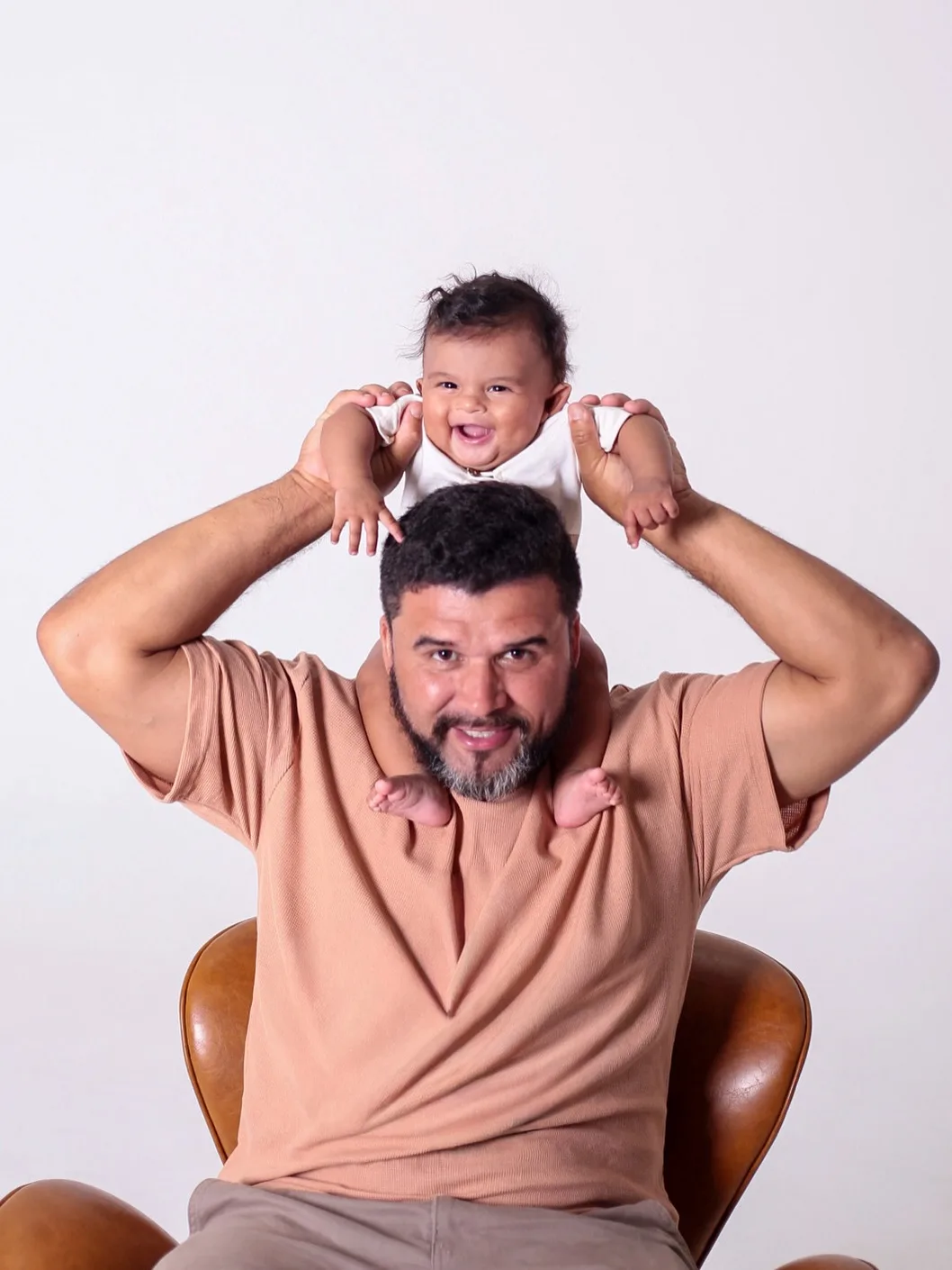 Pai sorri com o bebê sentado nos ombros.